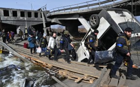 Ukrainian police officers help residents to cross a destroyed bridge as they evacuate Irpin, northwest of Kyiv, on 12 March 2022.