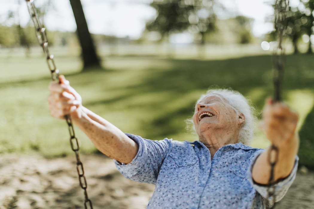 Cheerful senior woman on a swing at a playground