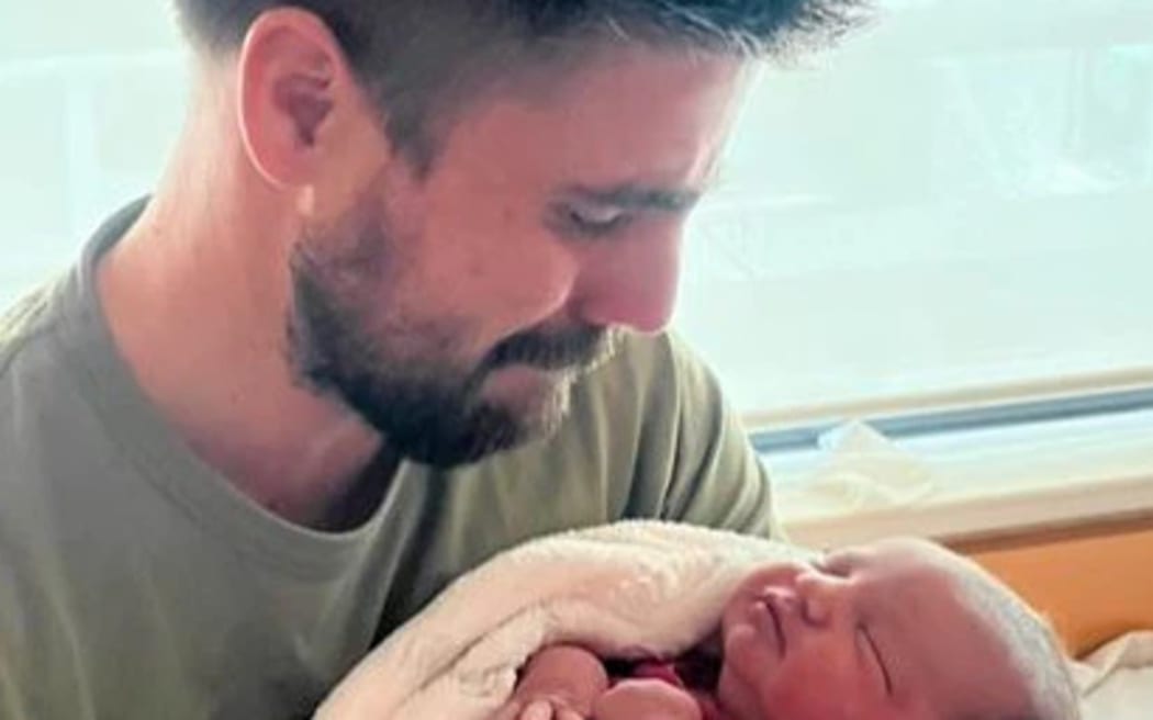 A man close to tears cradles a newborn baby.
