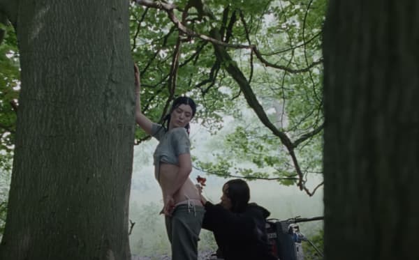 Alma Proença holds her tattoo tools on Lorde who is standing by a tree.