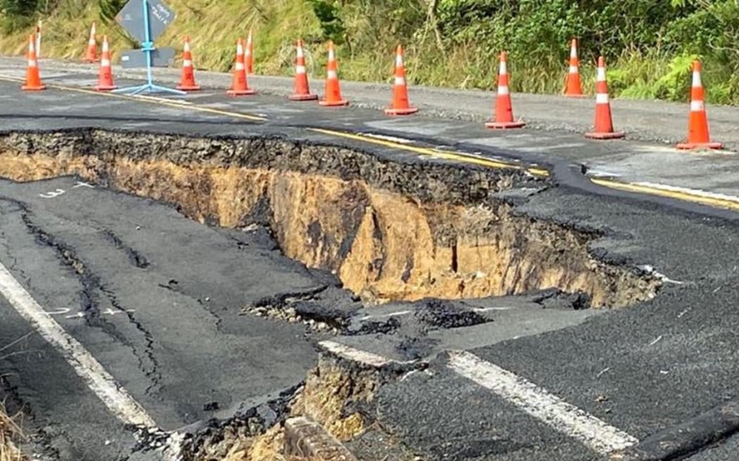 A photo of damage to the state highway shows cracking and slumping in the road with road cones around it.