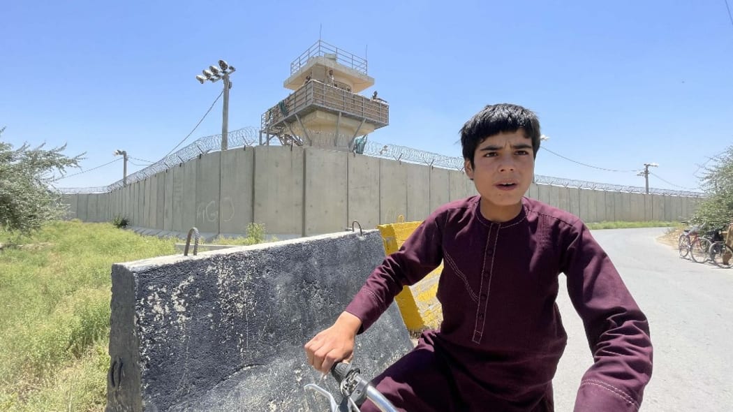 An Afghan boy cycles on a roadside behind the Bagram airfield while Afghan forces guard base towers in Kabul, Afghanistan.
