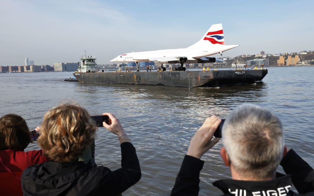 NEW YORK, NEW YORK - MARCH 14: People watch as retired British Airways Concorde supersonic airliner is moved by a barge on the Hudson River on March 14, 2024 in New York City. The Concorde, one of a fleet of seven once owned by British Airways, departed the Weeks Marine in Jersey City, N.J. for its return to the Intrepid Museum following a months-long restoration project at the Brooklyn Navy Yard.  (Photo by Michael M. Santiago/Getty Images)