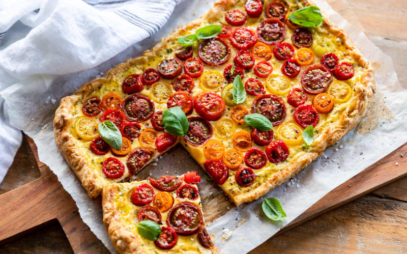 A pastry tart covered in cherry tomatoes and basil leaves.