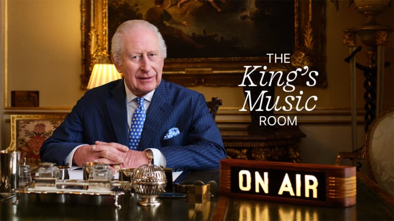 King Charles sits in his office in Buckingham Palace, an 'ON AIR' sign to his right and a graphic reading 'The King's Music Room' next to him.
