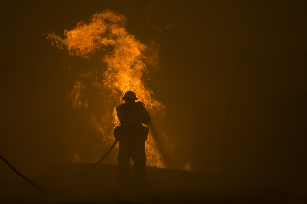 A firefighter hoses down burning pipes near a water tank at the Sand Fire near Santa Clarita, California.