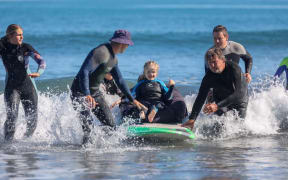 Livvy Kay on a surfboard in the ocean with volunteers helping her.