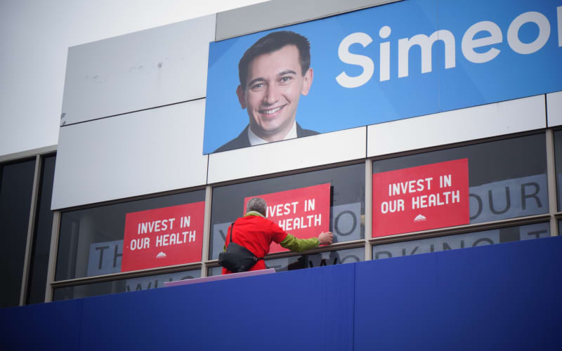 One of the protestors outside Simeon Brown’s electorate office has used a ladder to cover the Health Minister’s message in his window with their own placards.