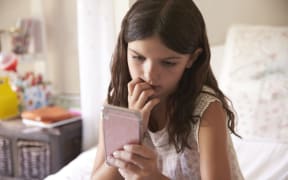 A photo of a young Girl In Bedroom Worried by what she's looking at on her phone