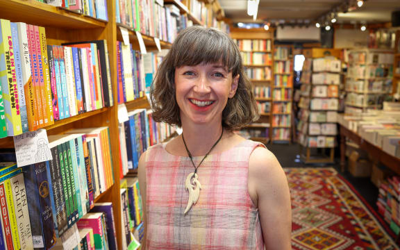 Jenna Todd is standing in the Mt Eden bookshop Time Out. She is surrounded by bookshelves.
