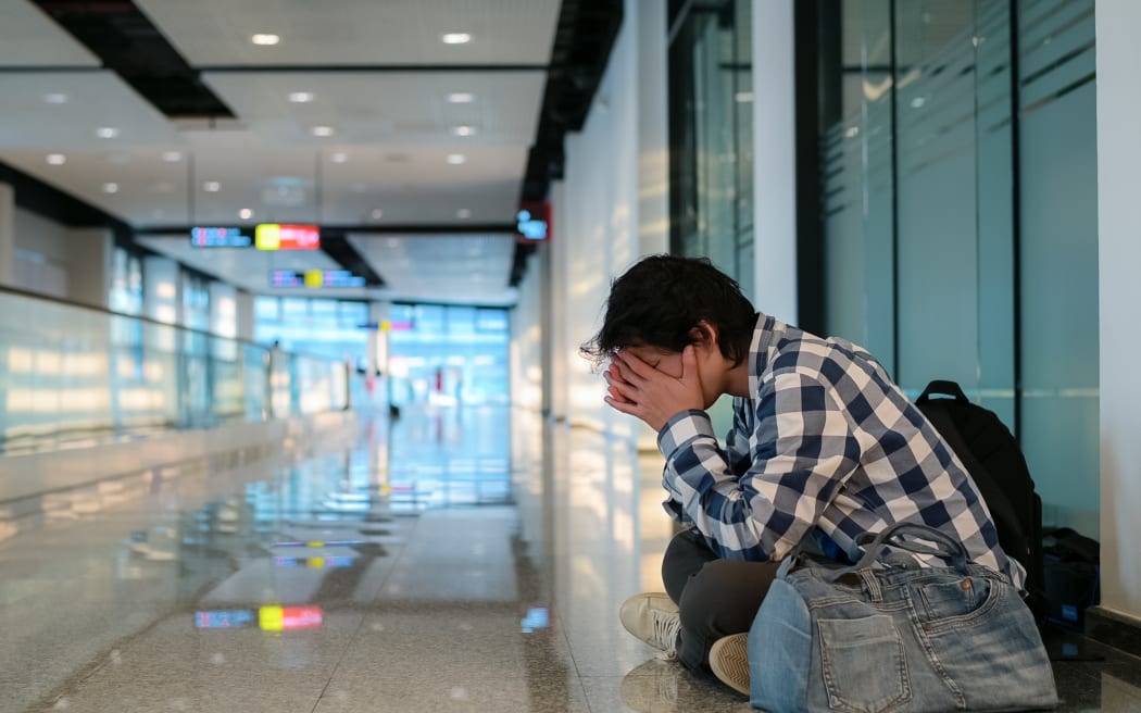 Man sitting on floor in public path way. He holding hand on head and bag feeling distress and stress because haven't been able to apply to unemployment.