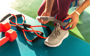 Woman putting on ankle wights before she starts a workout in a gym.