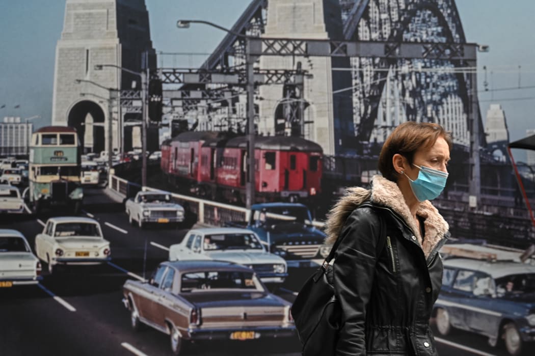 A woman wearing a mask walks past an image of the Sydney Harbour Bridge.