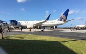 Passengers and flight crew who slept on a grounded United Airlines plane (rear) because of a Marshall Islands Covid-19 ban on incoming travelers deplane and walk to a rescue flight that arrived
Majuro shortly before 8am to collect the 124 passengers and flight crew.