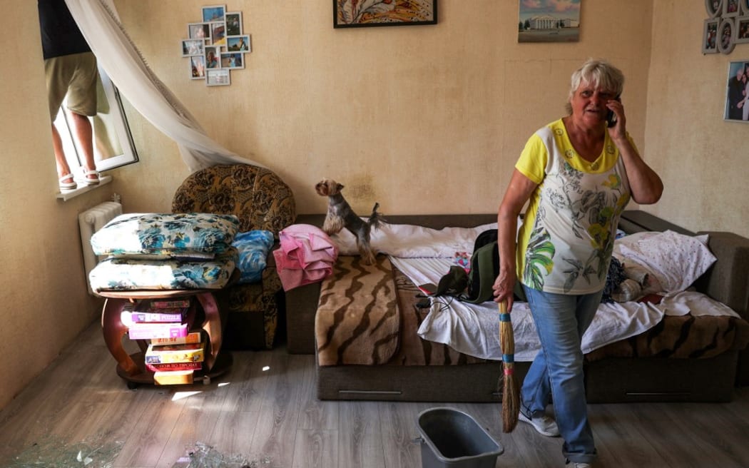 A woman speaks on her mobile phone as she cleans shattered glass from a broken window at her apartment, following a missile strike in Chernihiv, on August 19, 2023.