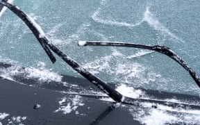 Windshield of car is covered with light snow and wipers are raised from glass.