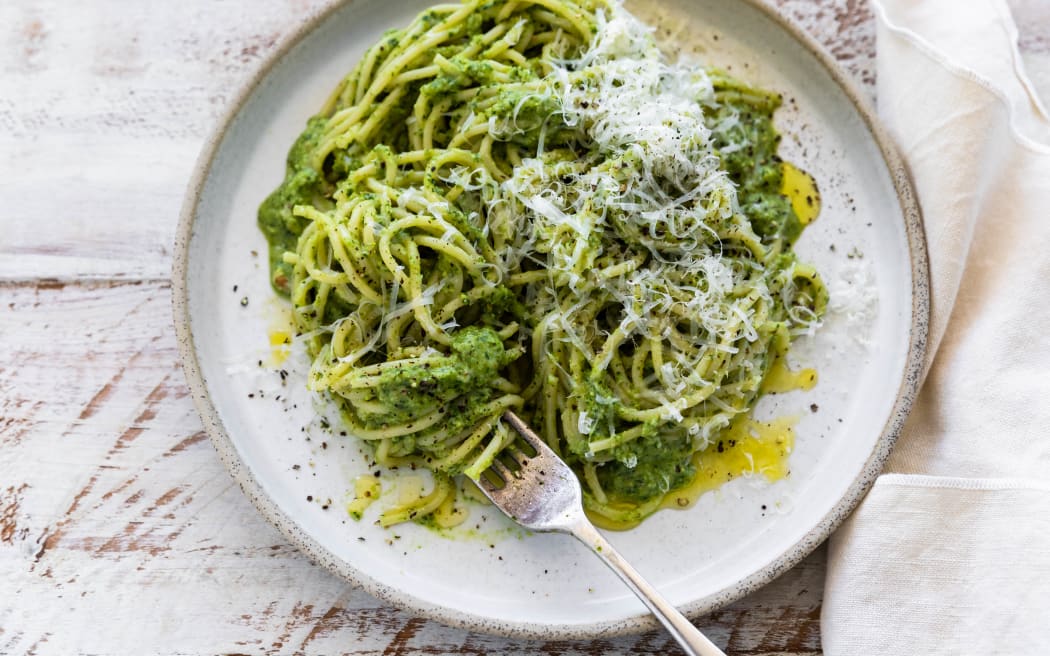 A dish of broccoli spinach pesto pasta garnished with grated parmesan.
