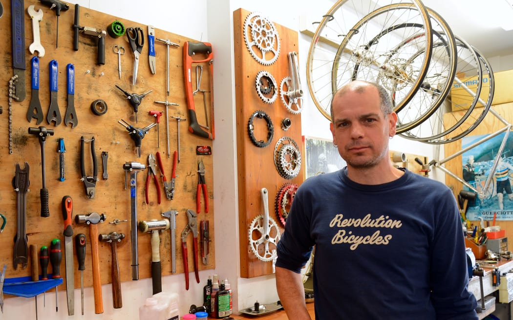 Owner in a bike shop surrounded by tools on board and hug up wheels