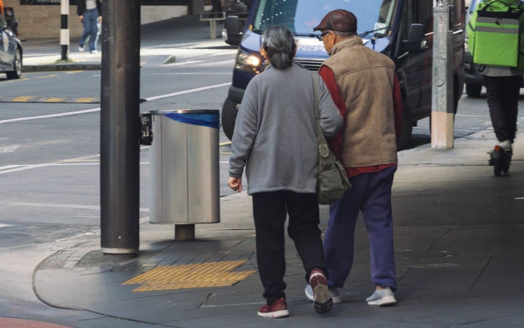 An elderly Chinese couple crossing the road on Queen Street in Auckland City.