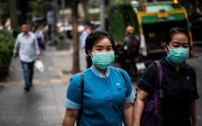 Pedestrians wearing face masks make their way along a street in Bangkok today.