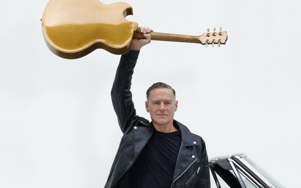 Musician Bryan Adams holding a guitar aloft