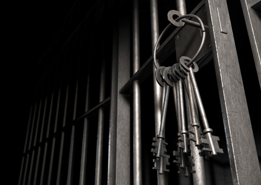 A closeup of the lock of a  jail cell with iron bars and a bunch of key in the locking mechanism with the door open