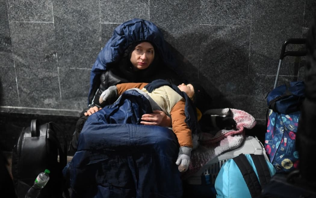 A woman holds her sleeping child while sitting on the ground at Lviv central train station in Western Ukraine on February 26, 2022.