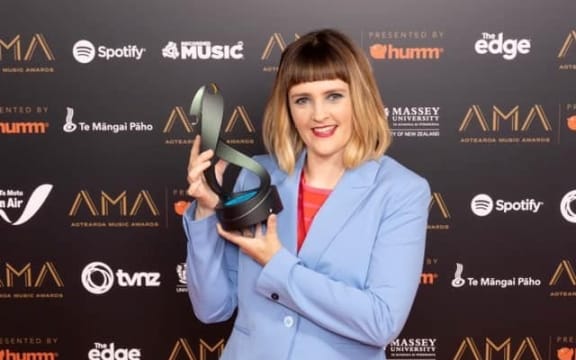 Composer Claire Cowan is wearing pale blue trousers and matching jacket. She's holding her Best Classical Artist Award at the Aotearoa Music Awards 2021.