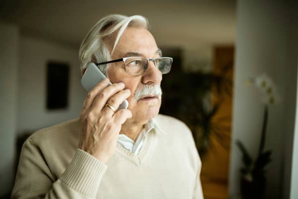 A senior man looks out the window as he talks on the phone.