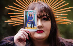Woman holds up a high priestess tarot card to cover her left eye.