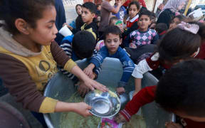 Palestinian children collect food at a donation point provided by a charity group in the southern Gaza Strip city of Rafah, on December 6, 2023, amid continuing battles between Israel and the Palestinian militant group Hamas. Israeli forces were encircling southern Gaza's main city of Khan Yunis on December 6, 2023, battling Hamas militants through streets and buildings in some of the most intense combat of the two-month war. (Photo by MOHAMMED ABED / AFP)