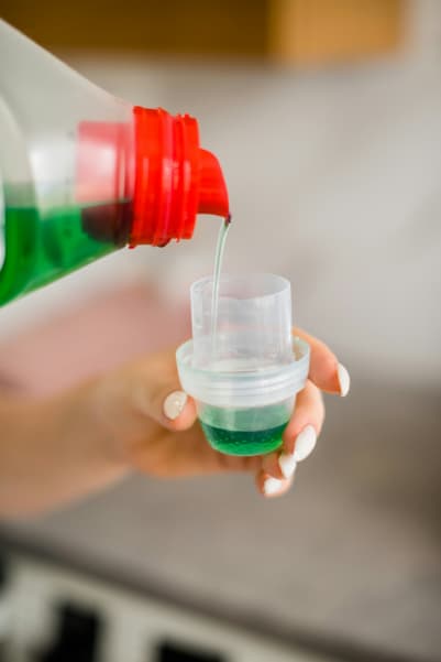 Person pouring green liquid detergent into the bottle cap.