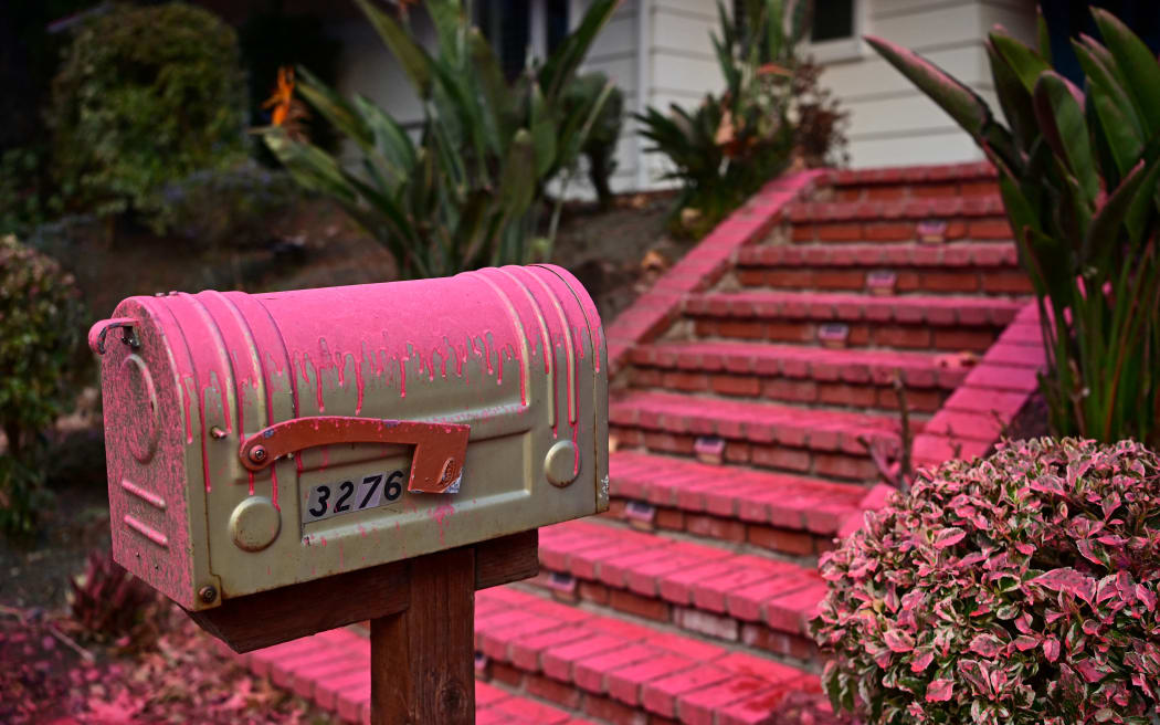 Red flame retardant is seen on the mailbox of a home in the Mandeville Canyon neighborhood of Los Angeles, California, on January 11, 2025, as the Palisades Fire continues to burn. The Palisades Fire, the largest of the Los Angeles fires, spread toward previously untouched neighborhoods January 11, forcing new evacuations and dimming hopes that the disaster was coming under control. Across the city, at least 16 people have died as multiple fires have ripped through residential areas since January 7, razing thousands of homes in destruction that US President Joe Biden likened to a "war scene." (Photo by AGUSTIN PAULLIER / AFP)