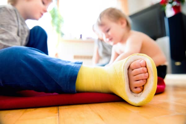 Child with a yellow coloured cast on their foot plays with another young child.
