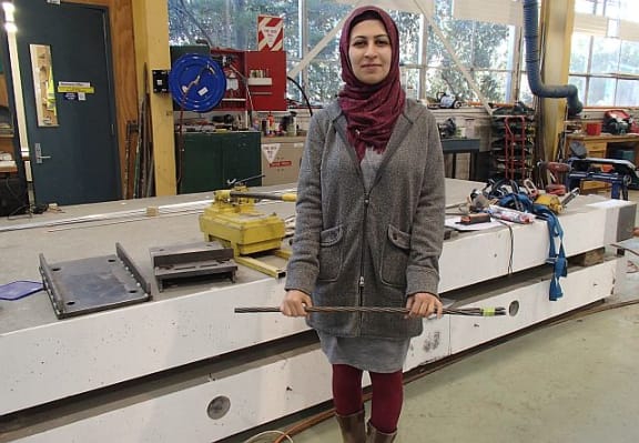 Engineering student Zeinab Chegini holds a short length of the wire cable that is used as a post-tensioning tendon. The tendons run the 10-metre length of each of the concrete slabs behind her, that make up the bridge superstructure.