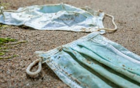 Green medical mask waste during COVID19. Discarded to ocean coronavirus single-use face masks. Environmental and coast plastic pollution. Trash in beach threatening the health of oceans