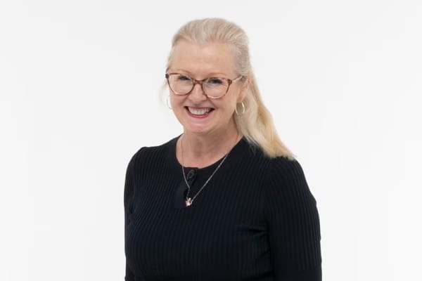 A smiling woman with long blonde hair and brown-framed glasses.
