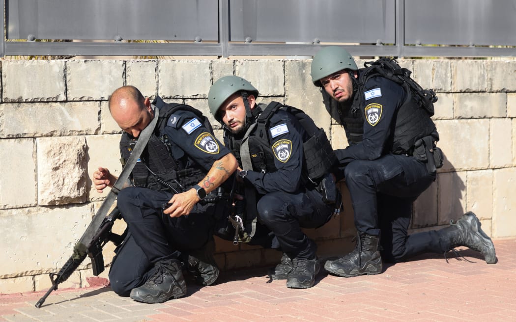 Members of the Israeli forces take cover on the side of a street in Ashkelon as sirens wail while barrages of rockets are fired from the Gaza Strip into Israel.