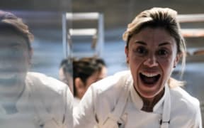 A smiling woman in a white chef's outfit paints uncooked croissants with a brush.