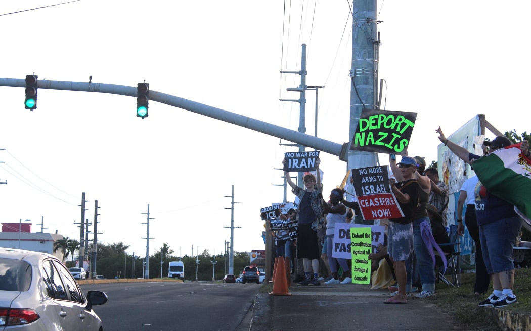 Demonstrators in Dededo, Guam, holding signs with various messages during the 2025 No King's rally.
