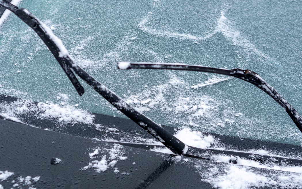 Windshield of car is covered with light snow and wipers are raised from glass.