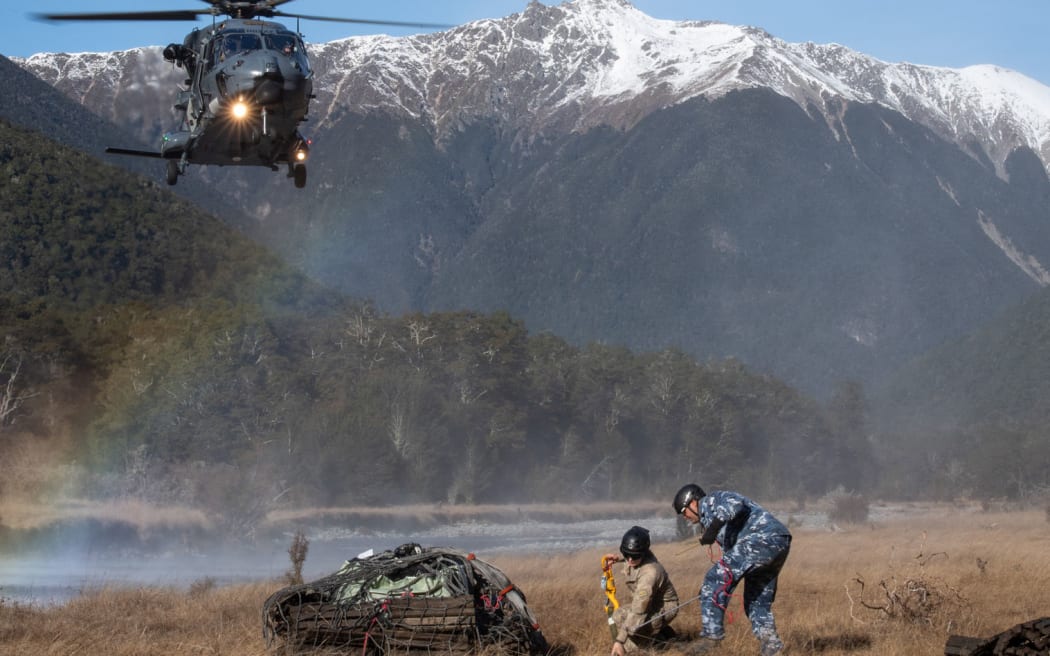 Nh90 Helicopter approaches the load ready for pick up while the team on the ground waits to hook the load onto the bottom of the helicopter.