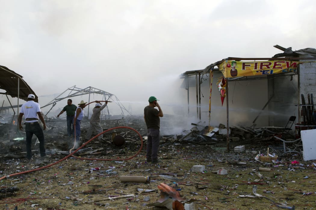 Firefighters and volunteers work amid the smouldering debris left by a blast in a fireworks market near Mexico City.