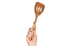A hand holds a wooden spatula high in the air.