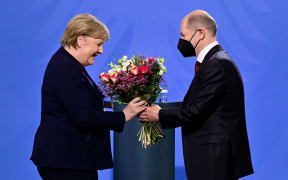 German Chancellor Olaf Scholz gives a bouquet of flowers to his predecessor Angela Merkel after she handed him over the office at the Chancellery in Berlin