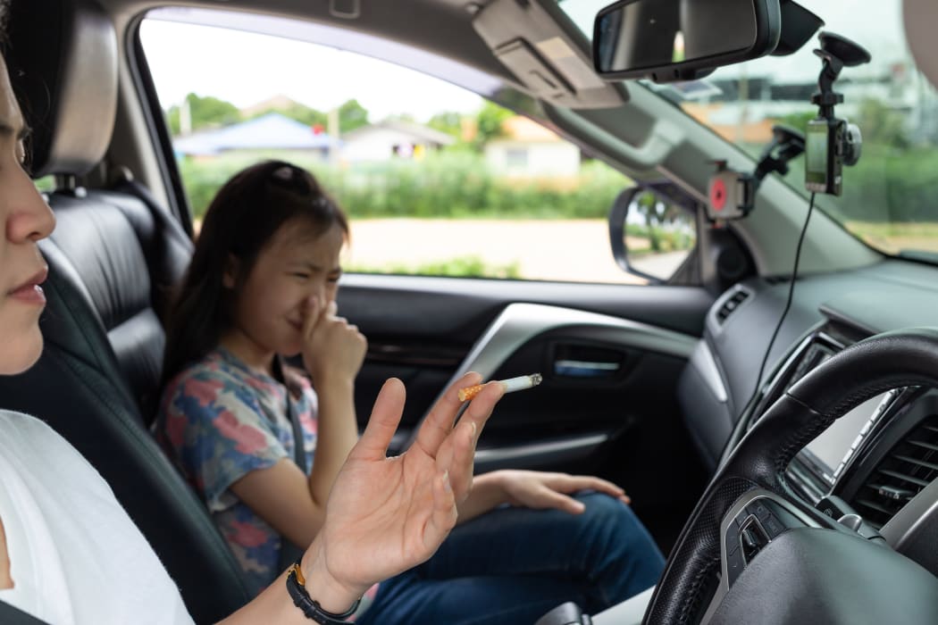 Woman smoking cigarette while driving inside the car and the child choking of smoke.