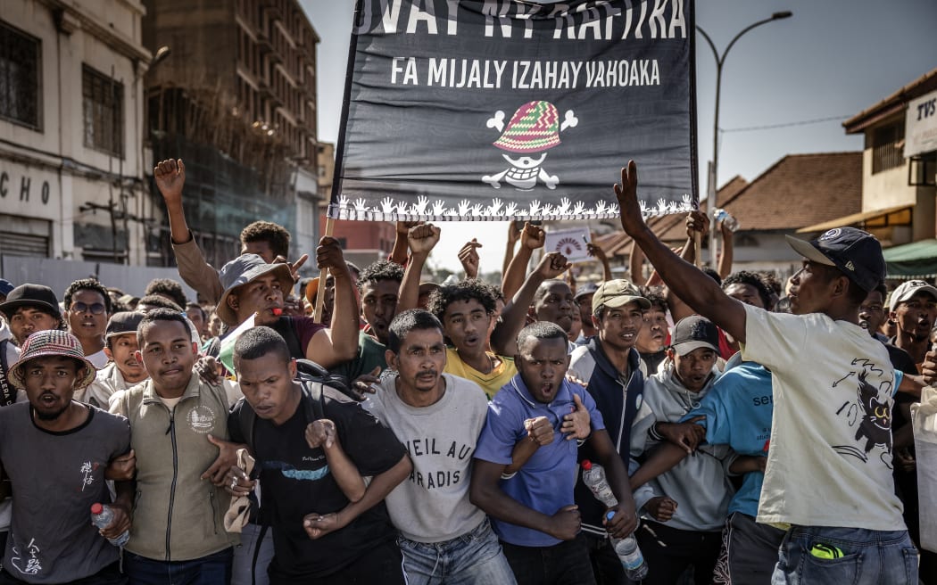 Protester chant anti-government slogans and hold a large banner featuring a Malagasy version of the logo of the popular Japanese manga One Piece, a symbol adopted by Gen Z protest movements worldwide, as they march from a civil society rally demanding the resignation of President Andry Rajoelina and paying tribute to the victims of the protests in Antananarivo, on October 13, 2025. Soldiers and security forces joined hundreds celebrating in Madagascar's capital on October 13, 2025, hours before President Andry Rajoelina was due to address the nation following weeks of protests and growing calls for his resignation. (Photo by Luis TATO / AFP)