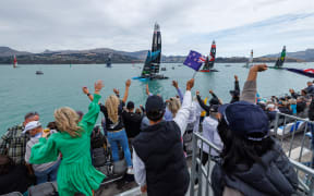 Spectators in the grandstand cheering the New Zealand SailGP Team as they wait on the water whilst the racing is on hold due to a dolphin sighting on the course on Race Day 1 of the ITM New Zealand Sail Grand Prix in Christchurch, New Zealand. Saturday 23rd March 2024. Photo: Brett Phibbs for SailGP. Handout image supplied by SailGP