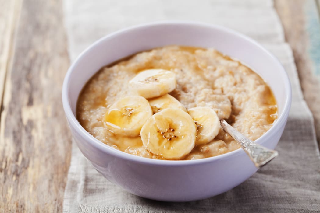 Bowl of oatmeal porridge with banana and caramel sauce on rustic table, hot and healthy breakfast every day, diet food