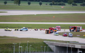 18 May 2024, Bavaria, Munich: Police and firefighters stand on a runway access road at Franz-Josef-Strauß Airport around climate activists who have stuck themselves there.  Climate protection activists paralyzed Munich Airport early Saturday morning. The activists had reached the inner area of the airport grounds. According to their own statements, members of the so-called Last Generation had planned to enter the airport grounds in order to block at least one of the two runways. Photo: Karl-Josef Hildenbrand/dpa (Photo by KARL-JOSEF HILDENBRAND / DPA / dpa Picture-Alliance via AFP)